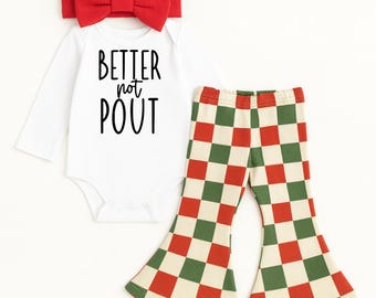 May include: A baby outfit set featuring a white long-sleeve bodysuit with the text "BETTER not POUT", a red bow headband, and checkered red, green, and cream bell-bottom pants. The outfit is designed for infants.