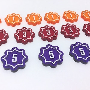 May include: A set of 12 plastic game tokens with a starburst design. The tokens are in three colors: orange, red, and purple. The numbers 1, 3, and 5 are printed on the tokens.