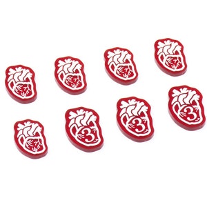 May include: Eight red heart-shaped tokens with white anatomical heart designs. Some tokens have the number "3" printed on them.