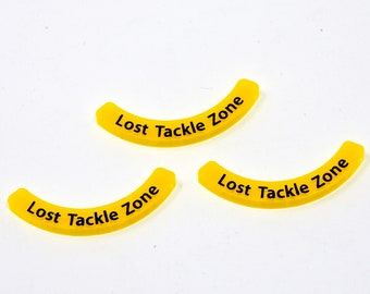 May include: Three yellow plastic game pieces shaped like a curved arc. Each piece has the text "Lost Tackle Zone" printed in black.