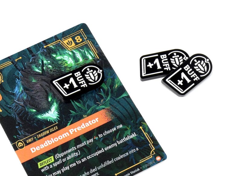 May include: A game card with the text "Deadbloom Predator" and three black and white "+1 BUFF" tokens. The card has a green and orange design with additional text. The tokens are rectangular with rounded corners.