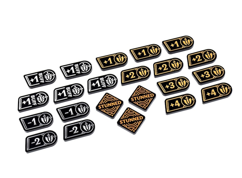 May include: A collection of black and gold game tokens with various markings. Some tokens have "+1 BUFF" and "+2" to "+4" symbols. Other tokens read "STUNNED" or "-1" and "-2". The tokens are likely used in a tabletop game.