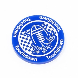 May include: A blue plastic game piece with a white design of a football, chequered flag, and grass. The text "Touchdown" is written around the edge of the piece.