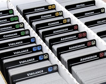 May include: A white divided storage box filled with stacks of black cards. Each card has a white label with text such as "Cunning", "Aggression", and "Vigilance". The cards are for a board game.