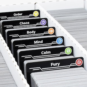 Könnte beinhalten: Eine weiße Aufbewahrungsbox aus Karton mit mehreren Stapeln von Spielkarten. Sechs schwarze Karten sind an der Vorderseite der Stapel sichtbar, beschriftet mit Order, Chaos, Body, Mind, Calm und Fury, jede mit einem farbigen Symbol.