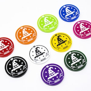 May include: Ten round tokens with a wizard hat design. The tokens are in various colors including red, orange, yellow, green, blue, purple, white, and black.