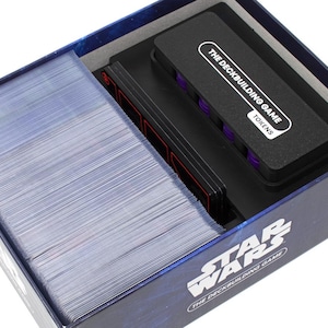 May include: A Star Wars The Deckbuilding Game box containing a large stack of clear plastic card sleeves and a black rectangular token storage tray. The tray lid features the white text THE DECKBUILDING GAME TOKENS and holds purple tokens.
