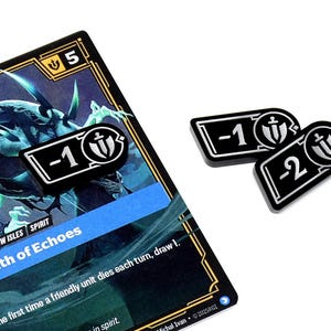 May include: A card game card with the text "Wraith of Echoes" and two black and white tokens. The card has a blue and black design with the number 5 in the corner. The tokens are rectangular with the numbers -1 and -2.