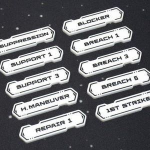 May include: White game tokens with black text, including "SUPPRESSION", "BLOCKER", "BREACH 1", "SUPPORT 1", "BREACH 3", "SUPPORT 3", "BREACH 5", "H. MANEUVER", "REPAIR 1", and "1ST STRIKE". The tokens have a black border and are on a black surface.