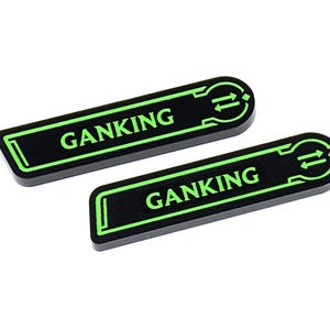 May include: Two black rectangular stickers with rounded ends. The word "GANKING" is printed in bright green, along with a green arrow symbol. The stickers are on a white background.