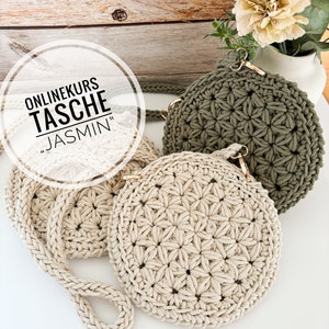 以下が含まれることがあります： 星形の模様が施された、かぎ針編みで作ったバッグが2つ。1つはベージュ、もう1つは緑色。バッグには金色の金属製の留め具と、長いベージュ色のかぎ針編みのストラップが付いています。白い円の中に「ONLINEKURS TASCHE "JASMINE"」という文字があります。