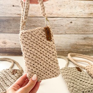 Peut inclure: Sac bandouli&egrave;re pour t&eacute;l&eacute;phone en crochet beige avec une bandouli&egrave;re tress&eacute;e et des accessoires dor&eacute;s. Le sac a une petite &eacute;tiquette en cuir marron. Plusieurs sacs sont visibles.