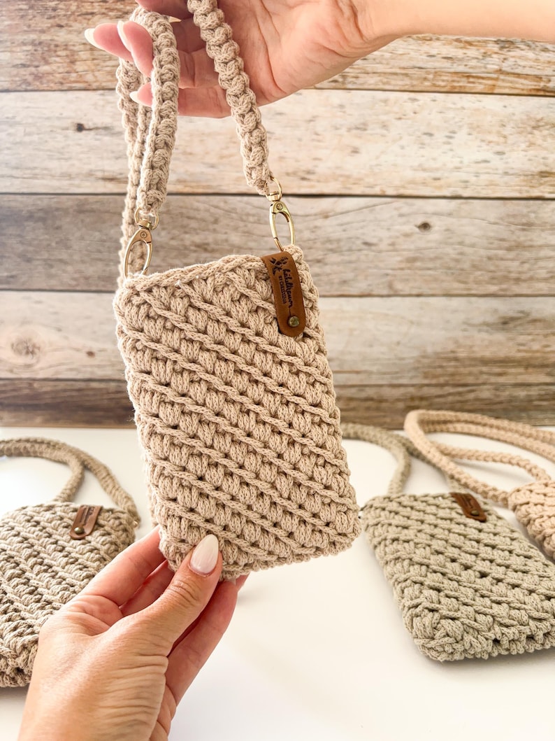 Peut inclure: Sac bandouli&egrave;re pour t&eacute;l&eacute;phone en crochet beige avec une bandouli&egrave;re tress&eacute;e et des accessoires dor&eacute;s. Le sac a une petite &eacute;tiquette en cuir marron. Plusieurs sacs sont visibles.