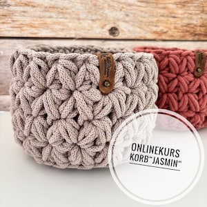 Könnte beinhalten: Zwei gehäkelte Körbe, einer in hellbeige und der andere in korallenrosa. Beide Körbe haben ein Leder-Etikett mit dem Text "Liebevoll Handgemacht" darauf. Der Text "ONLINEKURS KORB "JASMINE"" ist in einem weißen Kreis auf weißem Hintergrund geschrieben.