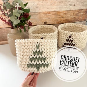 Pode incluir: Três cestas de crochê com fundo branco e um design de árvore de Natal verde e marrom. O texto "CROCHET PATTERN VIDEO SUBTITLES ENGLISH" está em um círculo branco.
