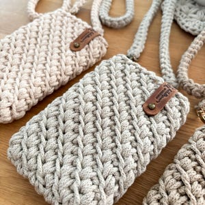Peut inclure: Gros plan sur plusieurs &eacute;tuis de t&eacute;l&eacute;phone crochet&eacute;s &agrave; la main dans des tons neutres. Chaque &eacute;tui a un motif de point textur&eacute;, une sangle assortie et une petite &eacute;tiquette en cuir. Les &eacute;tuis sont dans des tons beige et gris.