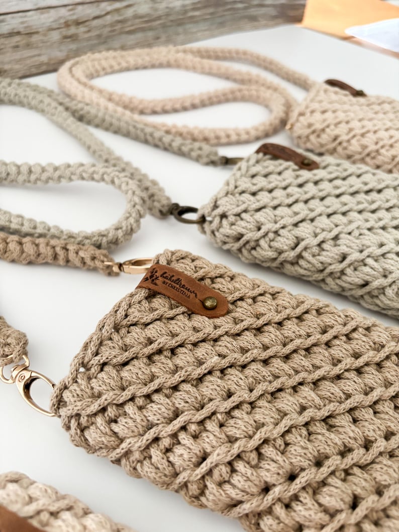 Peut inclure: Gros plan sur plusieurs &eacute;tuis de t&eacute;l&eacute;phone en macram&eacute; beige avec des lani&egrave;res assorties. Les &eacute;tuis pr&eacute;sentent un motif tiss&eacute; textur&eacute; et sont orn&eacute;s de petites &eacute;tiquettes en cuir marron. Les lani&egrave;res et les &eacute;tuis sont dans des tons beiges vari&eacute;s.