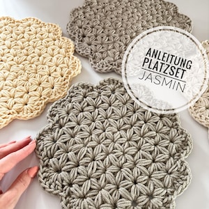 Peut inclure: Trois sets de table en crochet de couleur beige, beige clair et crème. Les sets de table sont réalisés avec un point étoile. L'image comprend le texte "Anleitung Platzset Jasmin".