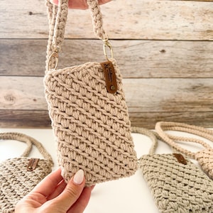 Pu&ograve; includere: Borsa a tracolla per telefono in crochet beige con cinturino intrecciato e hardware color oro. La borsa ha una piccola etichetta in pelle attaccata. Sono visibili diverse borse.