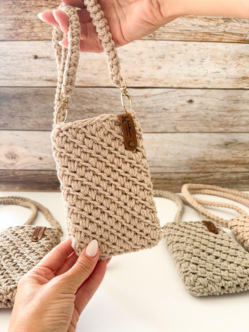Pu&ograve; includere: Borsa a tracolla per telefono in crochet beige con cinturino intrecciato e hardware color oro. La borsa ha una piccola etichetta in pelle attaccata. Sono visibili diverse borse.