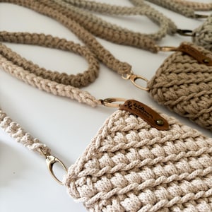 Peut inclure: Gros plan sur plusieurs &eacute;tuis de t&eacute;l&eacute;phone et lani&egrave;res en crochet faits &agrave; la main, dans des tons beige et marron. Les &eacute;tuis pr&eacute;sentent un motif textur&eacute; en point de bouclette, avec une &eacute;tiquette en cuir attach&eacute;e. Les lani&egrave;res ont des fermoirs m&eacute;talliques dor&eacute;s.