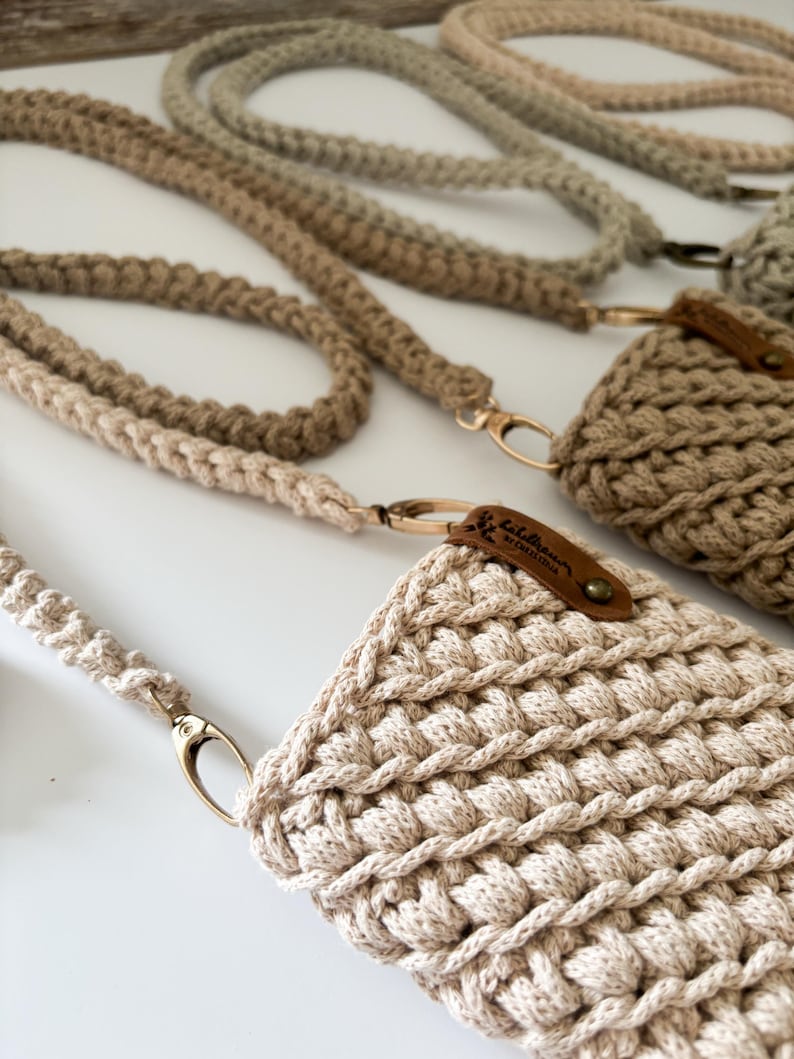 Peut inclure: Gros plan sur plusieurs &eacute;tuis de t&eacute;l&eacute;phone et lani&egrave;res en crochet faits &agrave; la main, dans des tons beige et marron. Les &eacute;tuis pr&eacute;sentent un motif textur&eacute; en point de bouclette, avec une &eacute;tiquette en cuir attach&eacute;e. Les lani&egrave;res ont des fermoirs m&eacute;talliques dor&eacute;s.