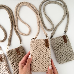 Peut inclure: Plusieurs &eacute;tuis de t&eacute;l&eacute;phone crochet&eacute;s aux tons neutres, beige et gris, avec des lani&egrave;res tress&eacute;es assorties. Chaque &eacute;tui est orn&eacute; d'une petite &eacute;tiquette en cuir et d'une quincaillerie dor&eacute;e. Pr&eacute;sent&eacute;s sur une surface blanche.