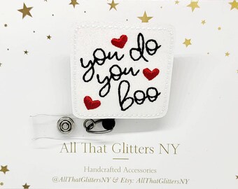 May include: White badge reel with the embroidered phrase "you do you boo" in black script and three red hearts. The badge reel has a clear plastic retractable cord and a metal clip.