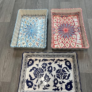 Puede incluir: Tres fuentes rectangulares de cerámica para hornear. Una fuente presenta un diseño floral azul y blanco, otra tiene un patrón geométrico rojo y blanco, y la tercera tiene un patrón floral azul y blanco. Cada fuente tiene un borde festoneado.