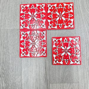 Op de afbeelding: Vier rode vierkante tegels met witte bloempatronen. De tegels zijn gerangschikt in een cluster, met een decoratief ontwerp. De tegels zijn waarschijnlijk voor woondecoratie of knutselprojecten.
