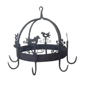 Puede incluir: Un colgador de ollas de hierro forjado negro con una parte superior abovedada y recortes decorativos de pájaros. El colgador tiene seis ganchos para colgar ollas y sartenes.