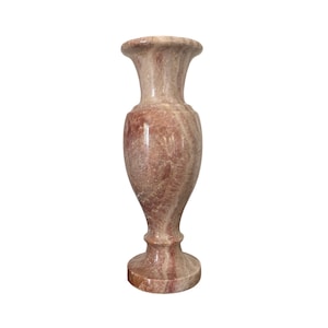 Puede incluir: Un jarrón de mármol rosa y blanco con un diseño clásico. El jarrón tiene una base ancha y un cuello estrecho.