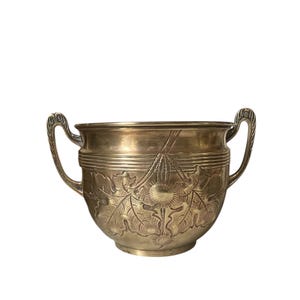 May include: A gold-toned metal serving bowl with two handles. The bowl has an embossed design of leaves and flowers.
