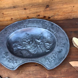 Peut inclure: Un plat ovale en argent avec un motif en relief de personnes et le texte "LE MELANOCENE DICQUEMARE  Etend les Cheveux de la Barbe LE ROUEN".