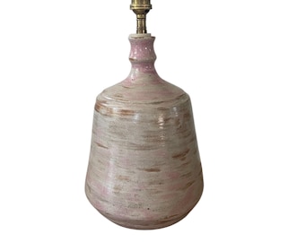 May include: A ceramic table lamp in pink and beige. The lamp features a rounded base and a narrow neck, finished with a brass lamp holder. The surface has a textured, hand-painted look, enhancing its unique, handcrafted charm. The lamp's height is approximately 25 cm.