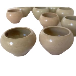 Peut inclure: Un ensemble de dix petits bols ronds en céramique dans différentes nuances de beige et de brun clair.