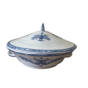 May include: A white ceramic serving dish with a lid, featuring blue floral patterns. The dish has two handles and a decorative finial on the lid. The rim and lid are adorned with a detailed blue border.