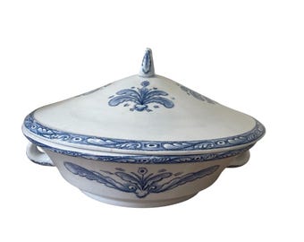 May include: A white ceramic serving dish with a lid, featuring blue floral patterns. The dish has two handles and a decorative finial on the lid. The rim and lid are adorned with a detailed blue border.