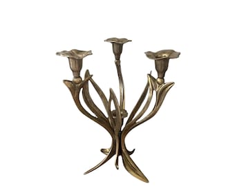 Könnte beinhalten: Ein dreiarmige Kerzenleuchter aus goldenem Metall mit floralem Design. Jeder Arm hat einen becherförmigen Kerzenhalter und ist wie eine stilisierte Blume geformt.