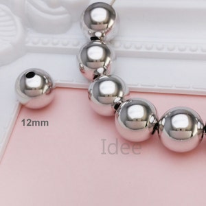 May include: A close-up of a strand of silver beads. The beads are round and smooth, and they are all the same size. The beads are 12mm in diameter. The beads are on a white background.