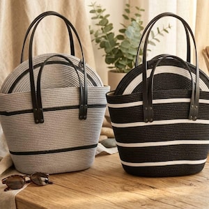 May include: Two woven tote bags with black leather handles. One is gray with black stripes, and the other is black with white stripes. Both bags contain matching sun hats. Sunglasses rest on the wooden surface.