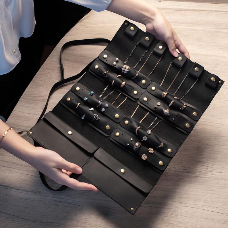 Elegant customizable leather jewelry case with multiple compartments. Perfect for organizing rings, necklaces, and bracelets while traveling. Made from genuine leather with a secure strap closure for safe storage.