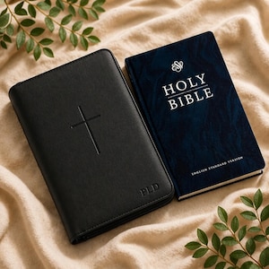 May include: A black leather-effect Bible cover featuring an embossed cross and the initials PLD, positioned next to a dark blue Holy Bible book with the text Holy Bible and English Standard Version printed in white on the front cover.