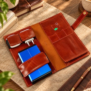 May include: A brown leather tech organizer case featuring multiple interior pockets and a strap closure. The organizer holds a bright blue rectangular power bank, two white wall chargers, and a small green SIM card tool within its stitched compartments.