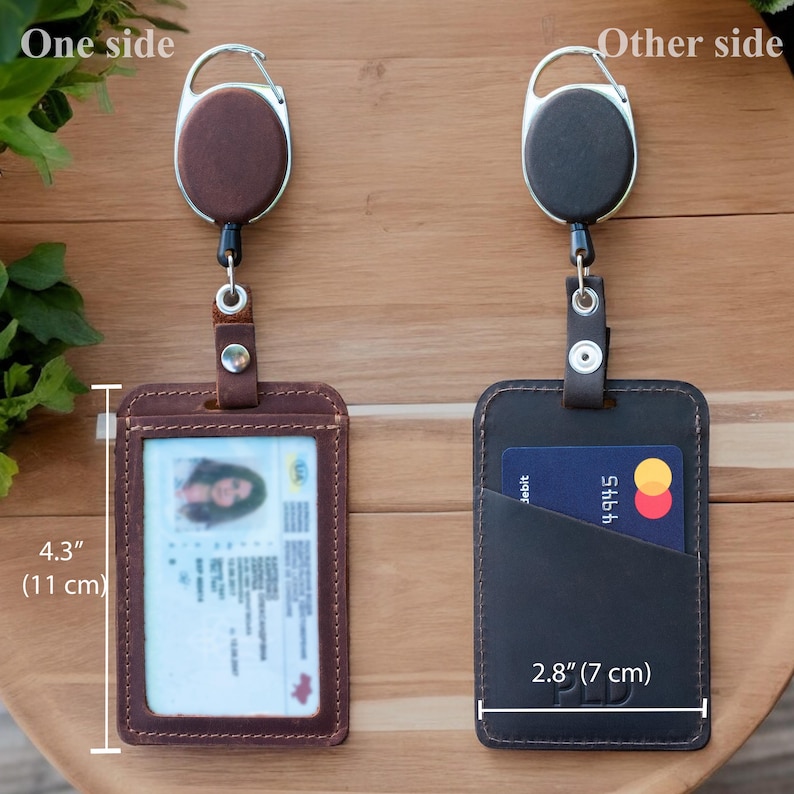 May include: Two leather badge holders with retractable reels. The left holder is brown with a clear window containing an ID card. The right holder is black with a card slot holding a debit card. Dimensions are 4.3 inches by 2.8 inches.