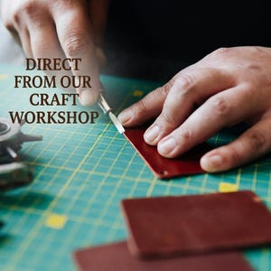 May include: A metal craft tool cutting a piece of dark red leather on a green cutting mat with grid lines. The text DIRECT FROM OUR CRAFT WORKSHOP is printed in brown letters on the left side of the image, positioned above the leather piece.