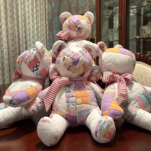 Può includere: Un gruppo di quattro orsacchiotti di peluche realizzati con toppe di tessuto trapuntato in vari colori e motivi pastello. Ogni orso presenta arti e busto trapuntati bianchi, orecchie arrotondate e un nastro di tessuto a righe rosse e bianche al collo.