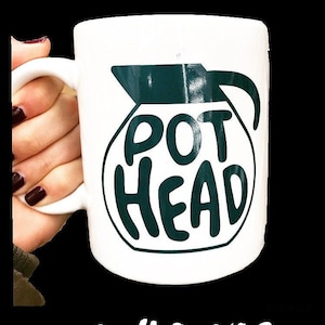 May include: White ceramic coffee mug with a green graphic of a coffee pot and the text "POT HEAD".