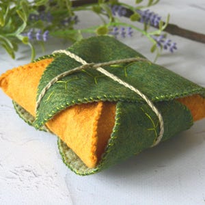 Op de afbeelding: Een klein, groen en oranje gevoerd zakje, vastgebonden met touw. Het zakje heeft een bladerenpatroon en is perfect om kleine spullen in op te bergen.