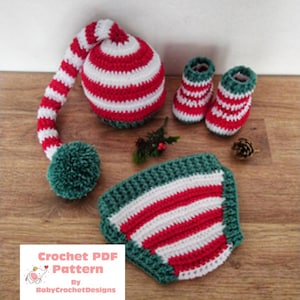 Op de afbeelding: Haakpatroon PDF voor een kerstmanmuts, slofjes en een slab. De muts heeft een lange, gestreepte staart en een groene pompon. De slofjes en de slab zijn rood-wit gestreept met groene afwerking. Het patroon is van BabyCrochetDesigns.